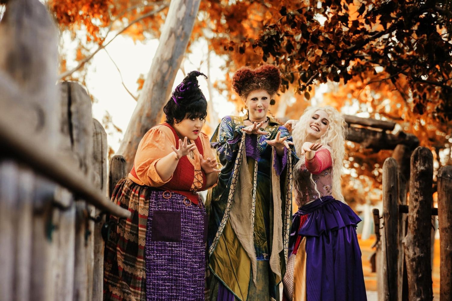 Group in Halloween costumes posing outdoors under orange autumn foliage.