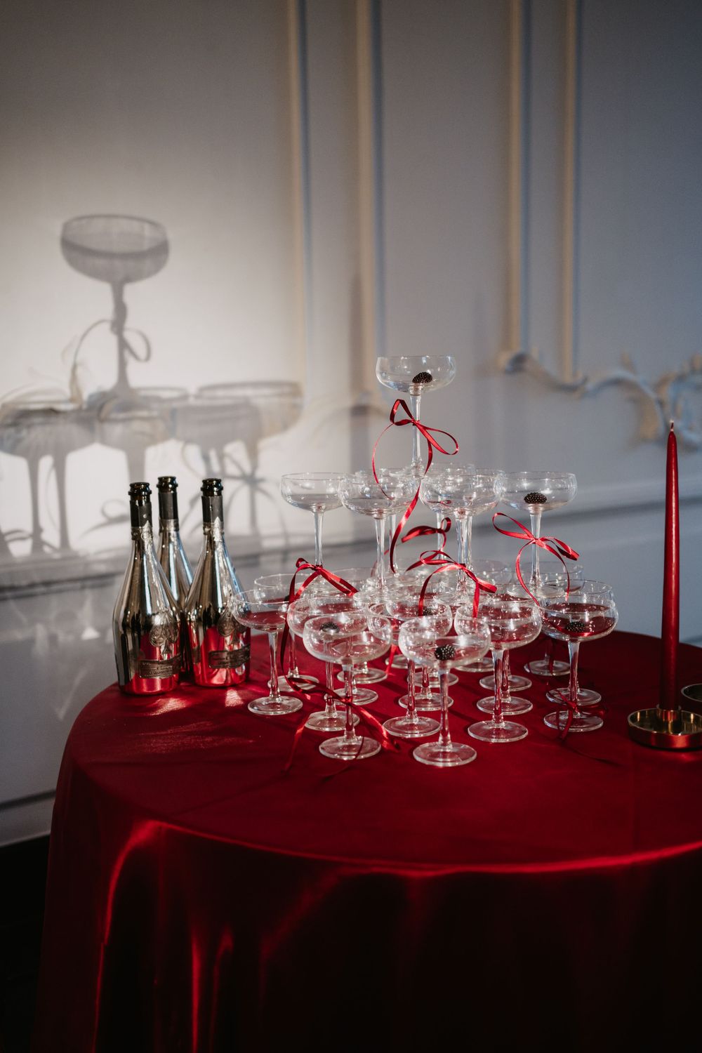 Champagne tower setup with coupe glasses on red velvet tablecloth with red candles.