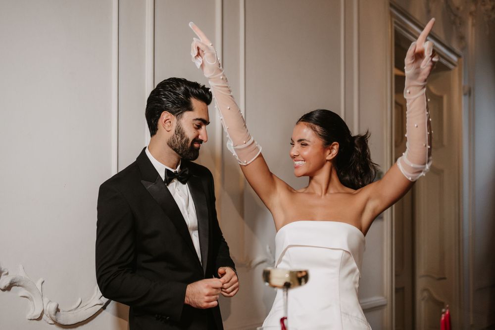 Couple celebrating with champagne as bride raises arms in joy.