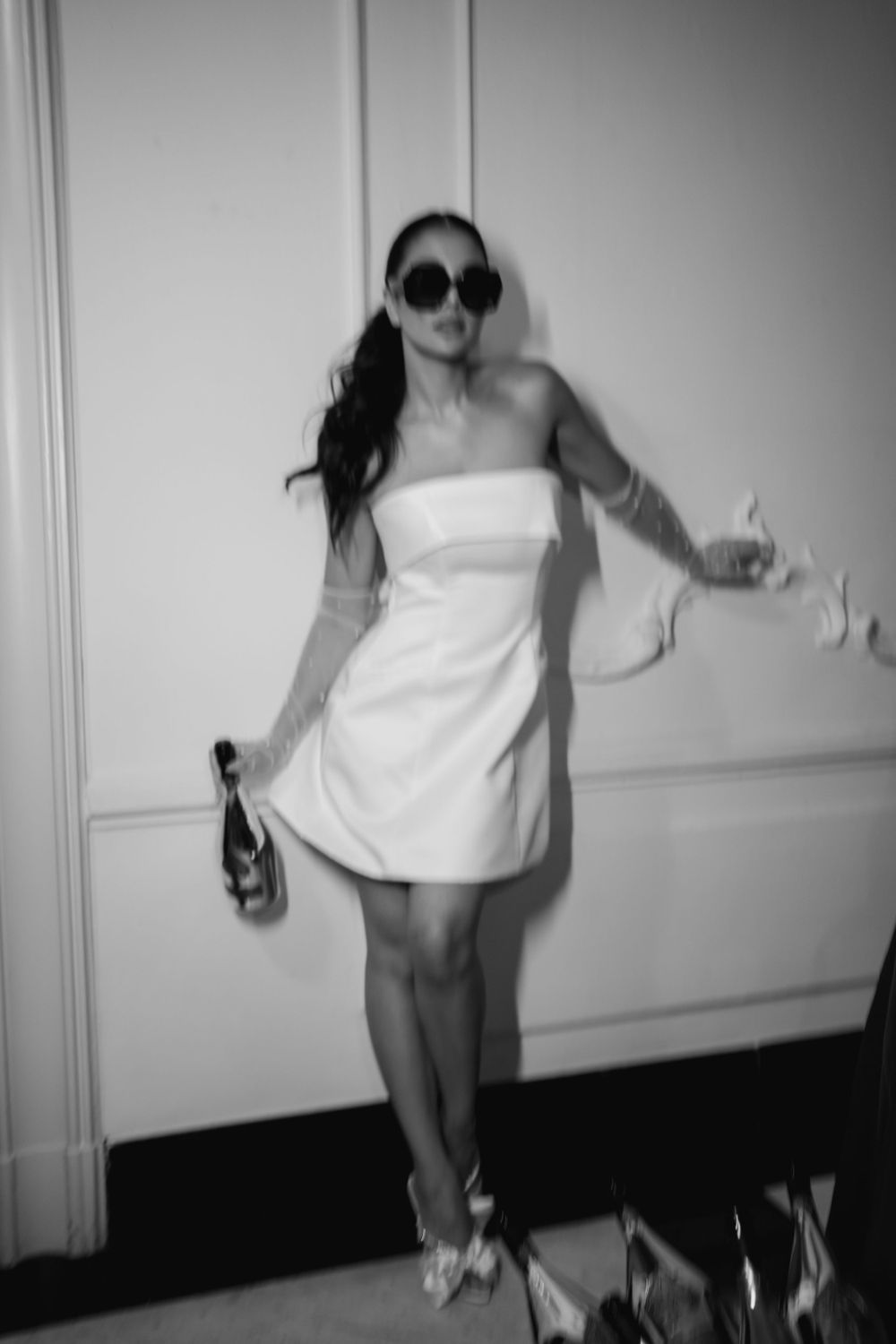 Black and white shot of bride posing with champagne bottle and sunglasses.