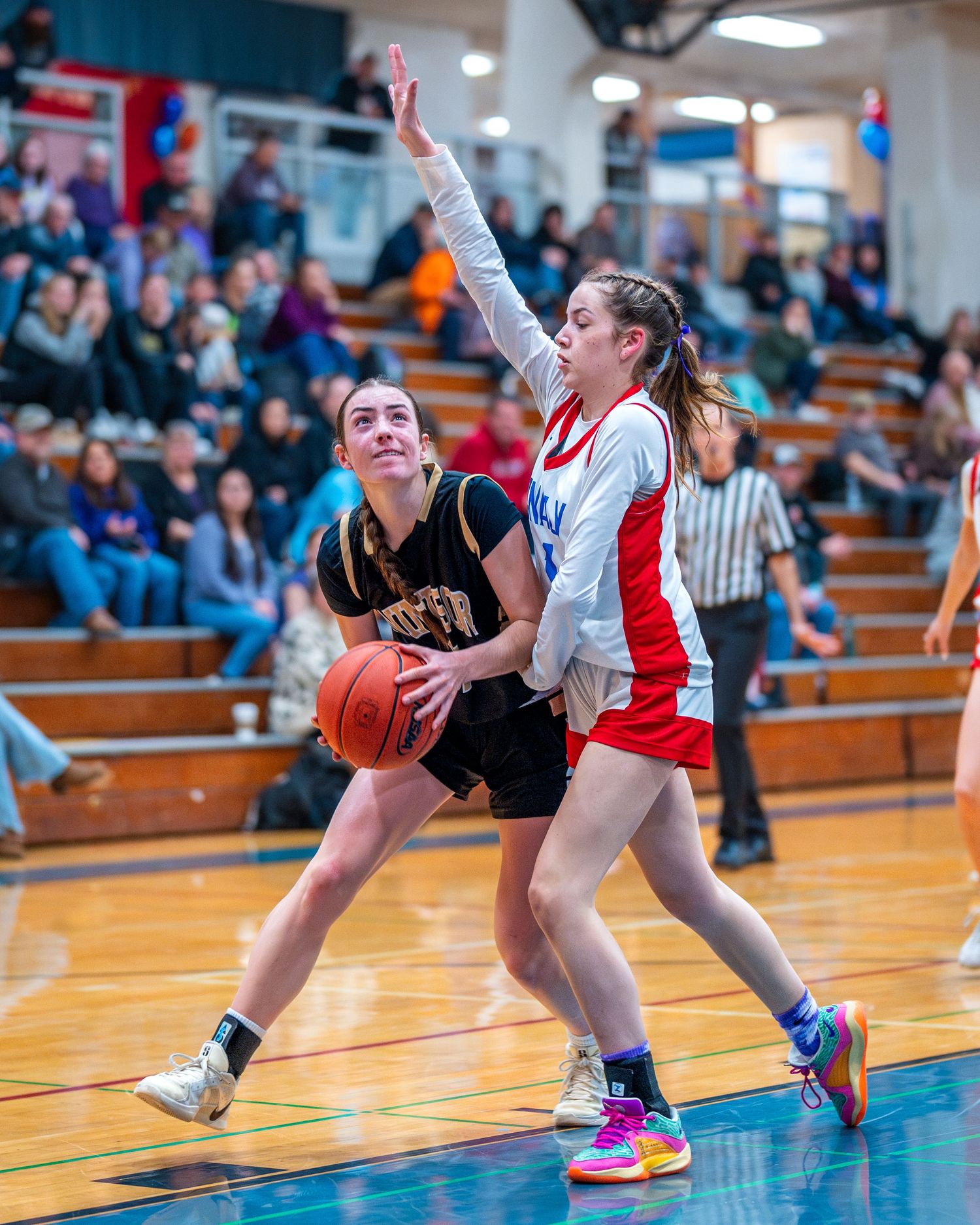 High school basketball players compete for the ball during an intense game in a gymnasium with wooden bleachers.
