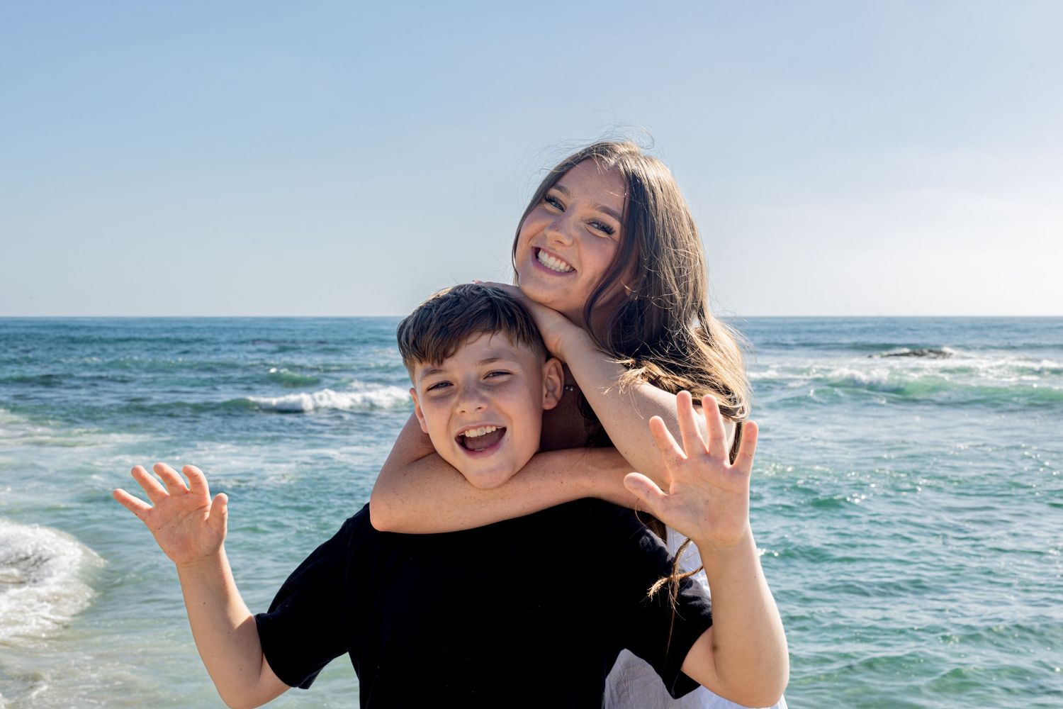San Diego family photography of a happy brother and sister hugging and smiling on the beach with the ocean background.