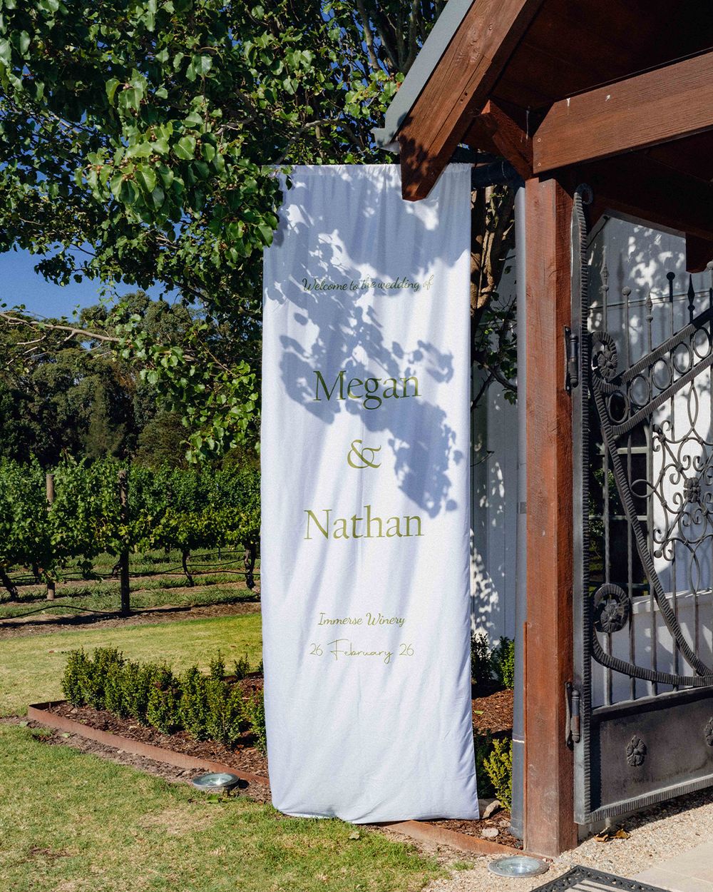 Elegant wedding banner for Megan and Nathan displayed at a vineyard venue entrance on a sunny day.