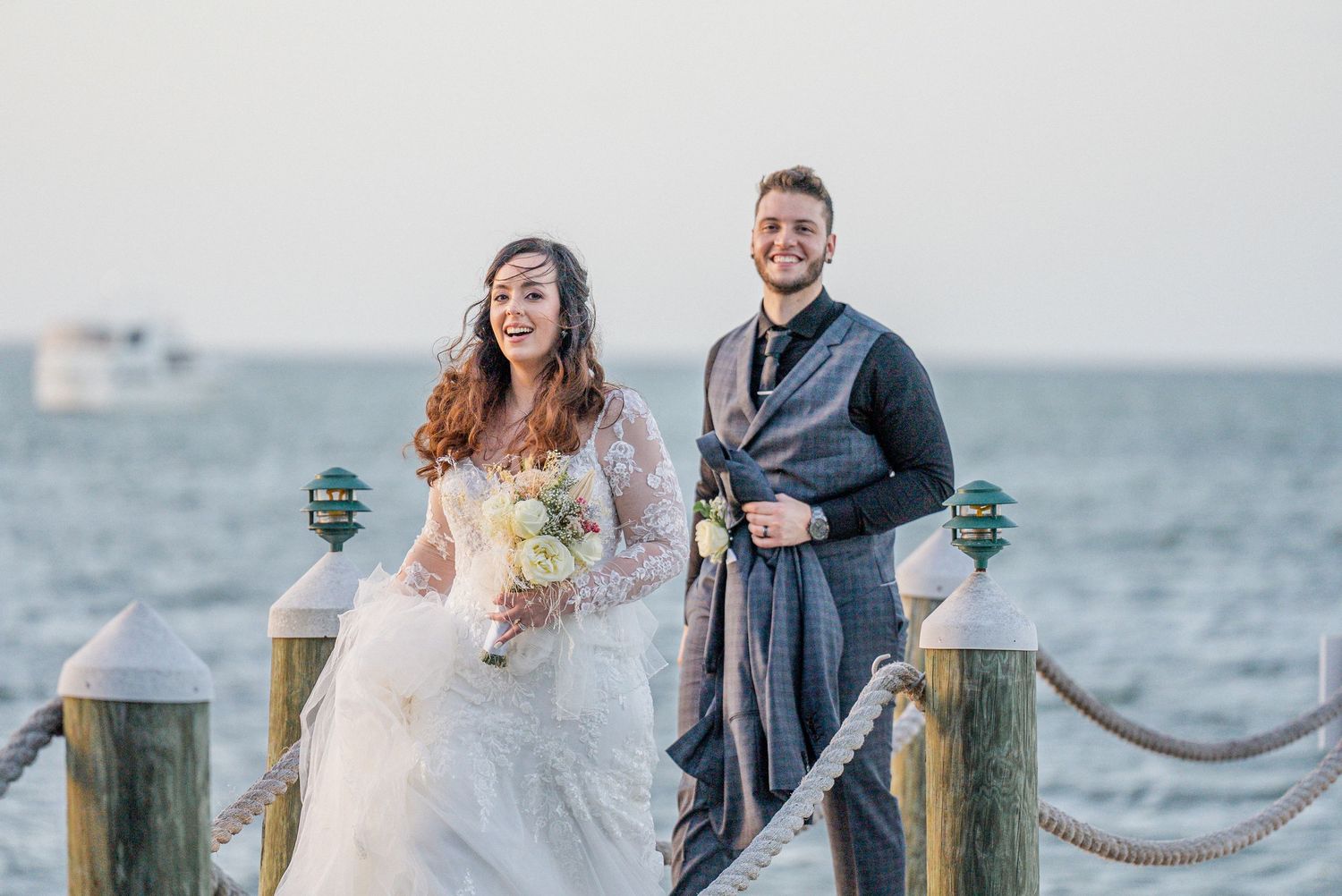 Wedding party celebrating and posing near wooden dock by the water at sunset.