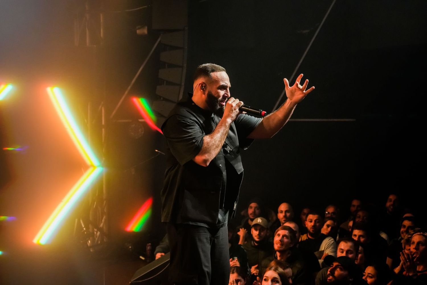Artiste face à la foule, éclairé par un V lumineux orange en arrière-plan