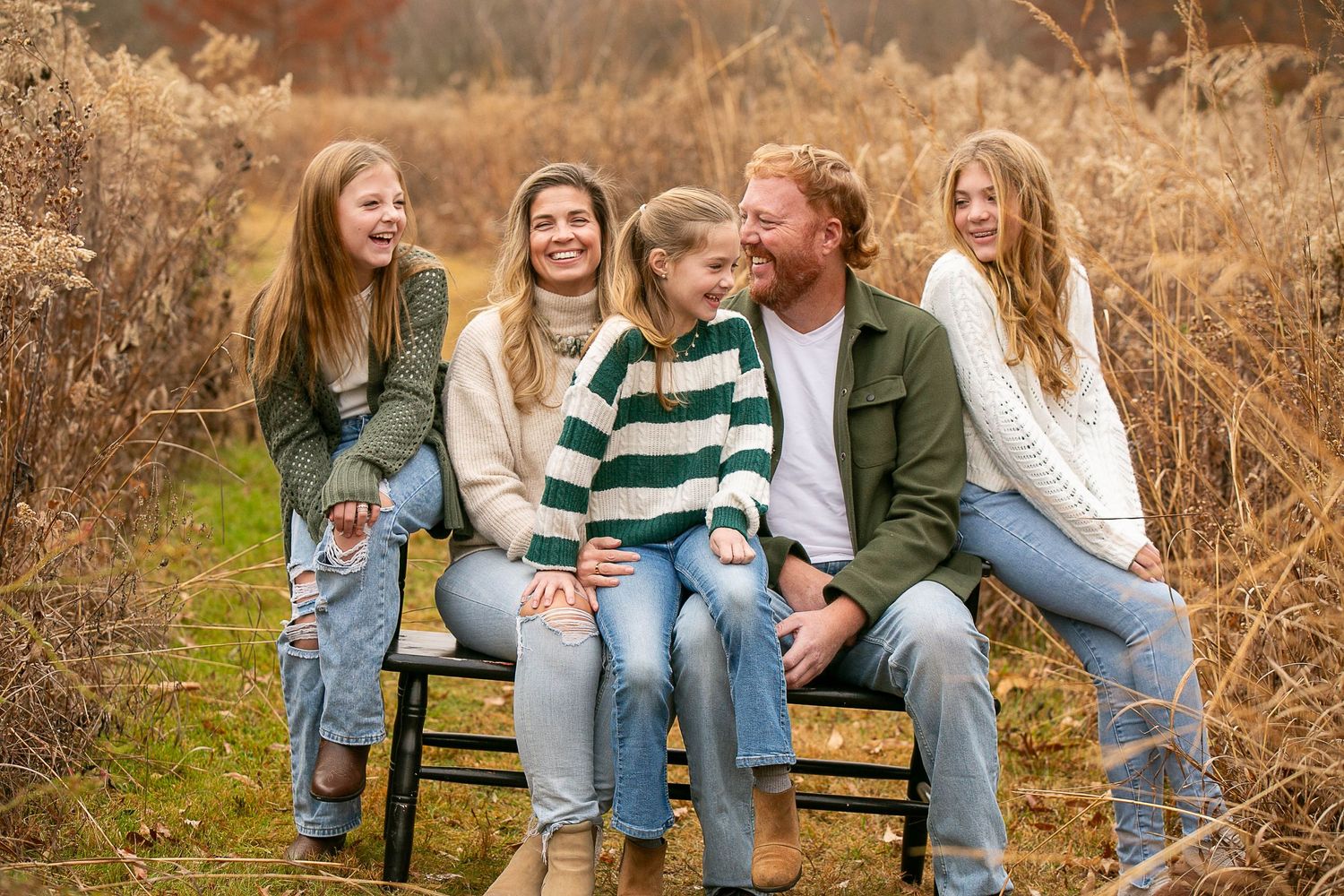 Family members sitting together on wooden bench during fall photo session.