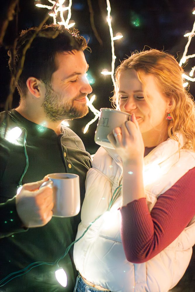 A couple is drinking hot chocolate with twinkle Christmas lights strung around them. Couple photography