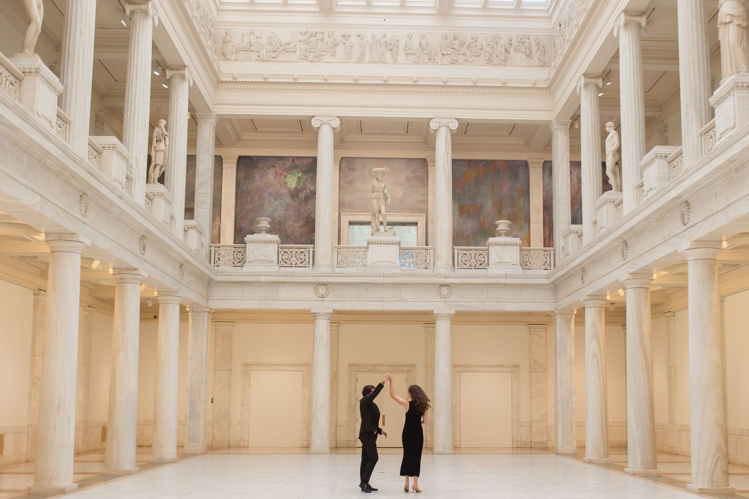 A grand white interior hall with classical columns and ornate ceiling details.