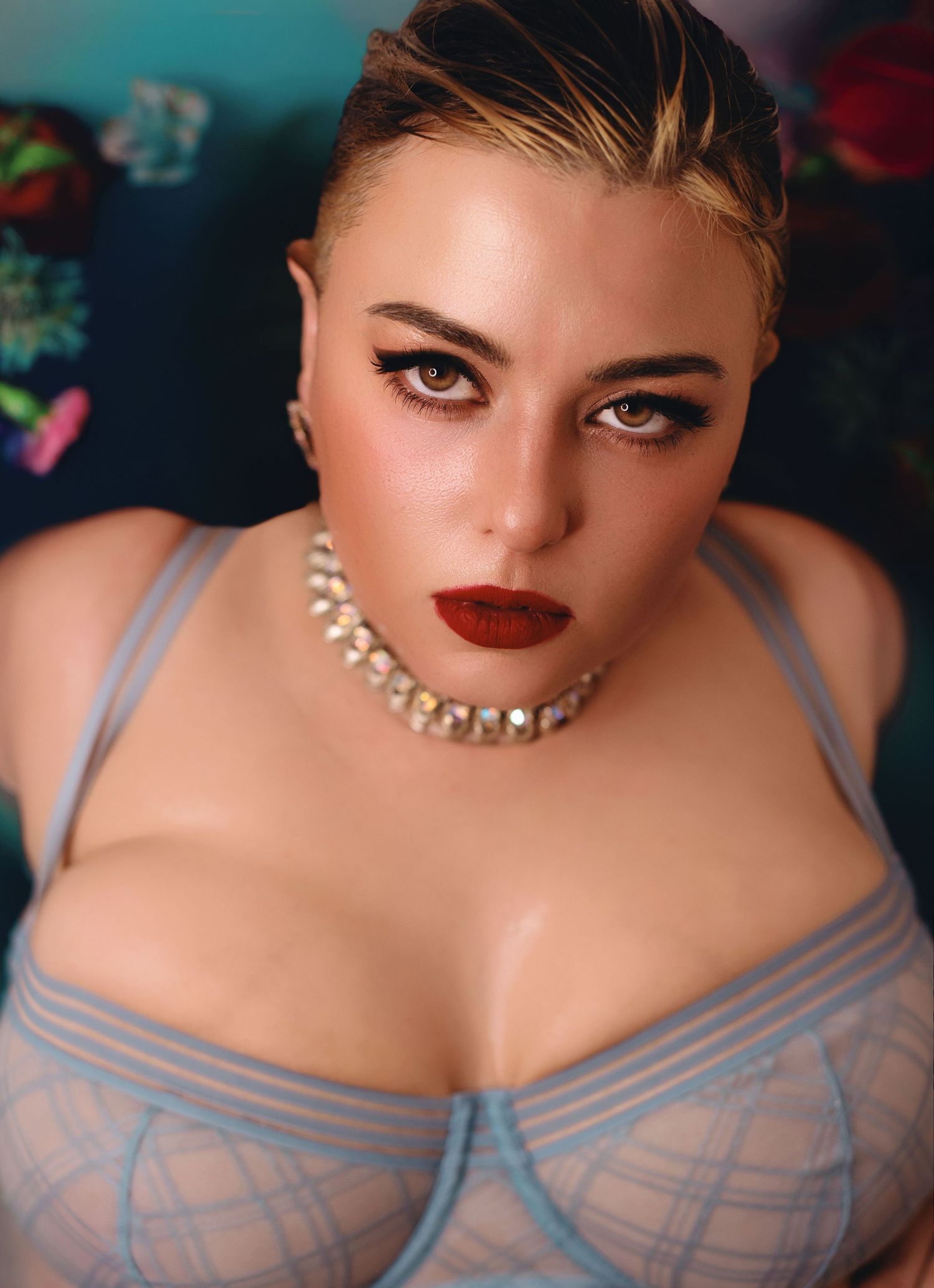 Portrait of someone wearing a pearl necklace and gray lingerie against a dark background with soft lighting and bold red lipstick.