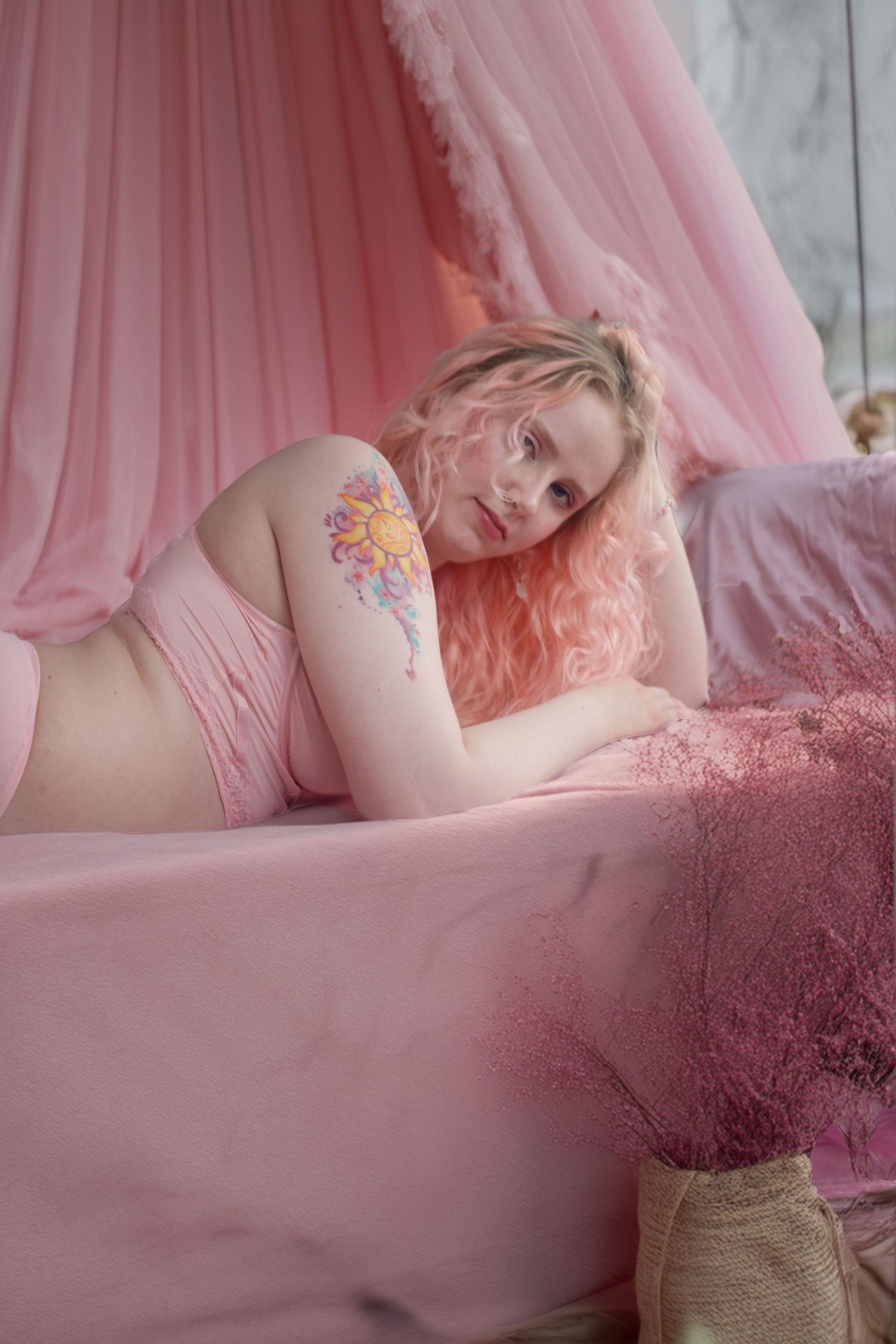 Ethereal boudoir photography featuring soft pink tulle fabrics and a colorful floral tattoo in dreamy lighting.