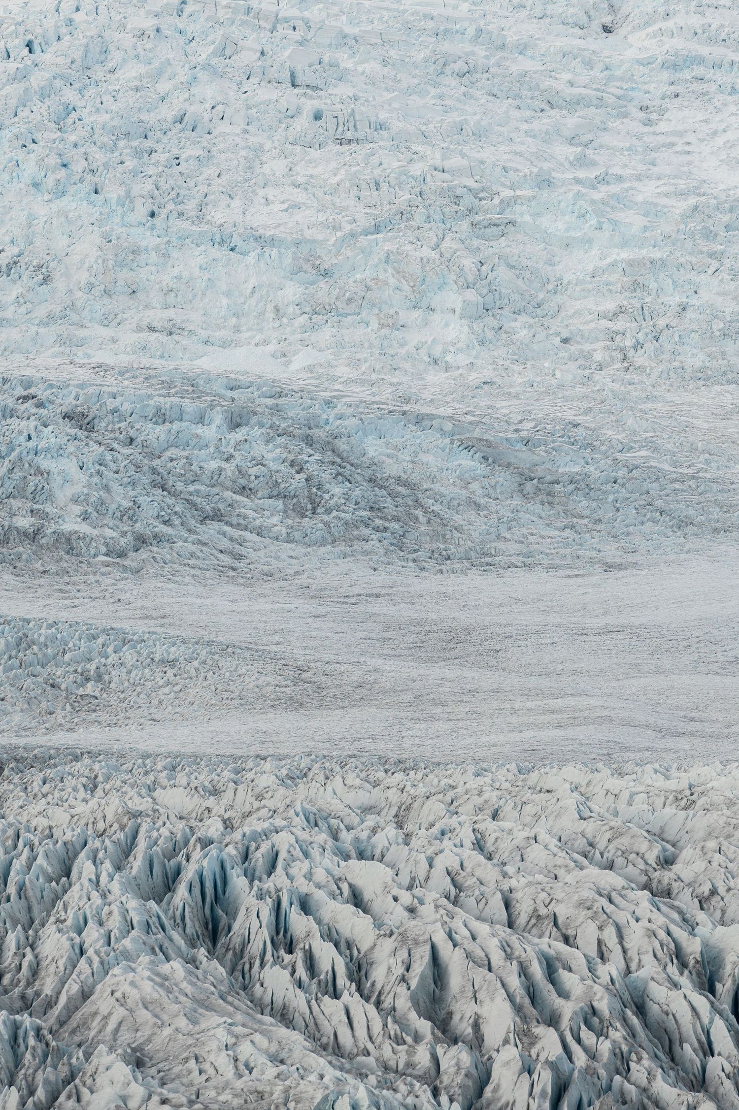 Textured surface of blue-white glacier ice formations in rugged terrain.