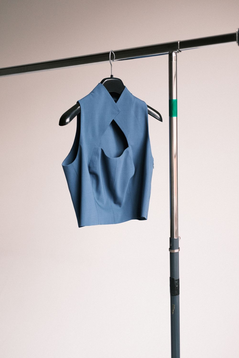 A sleeveless light blue crop top hangs on a black clothing rack against a white wall.