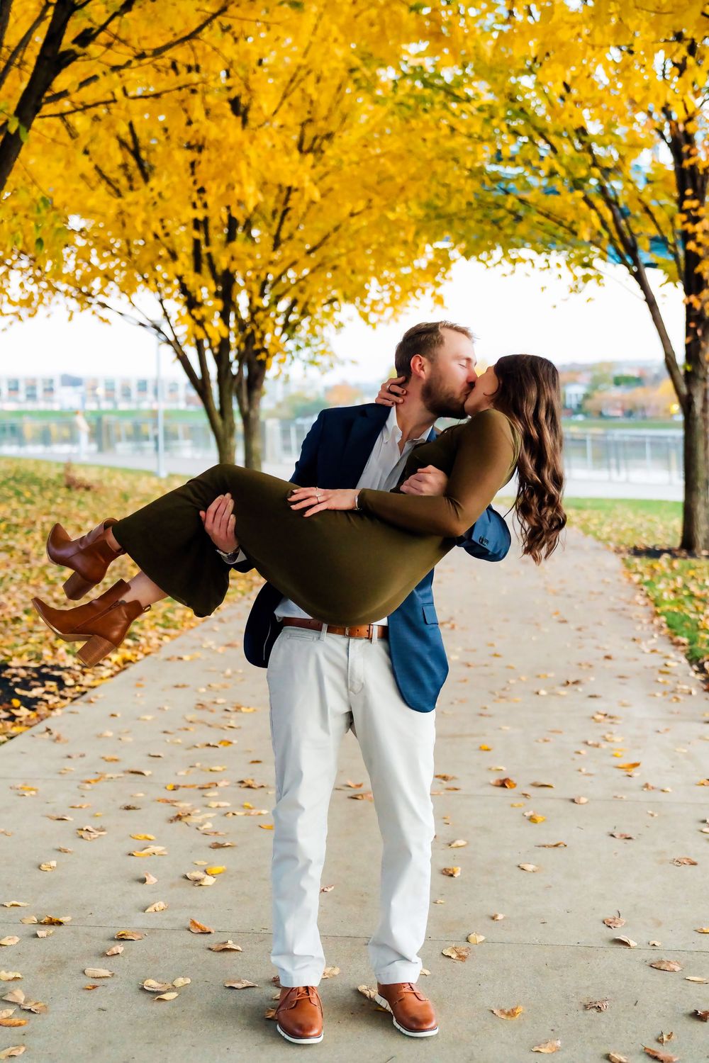 Liz and Chris's Engagement Downtown Cincinnati at Smale Park kissing while being held with fall leaves: Cincinnati Wedding Photographer