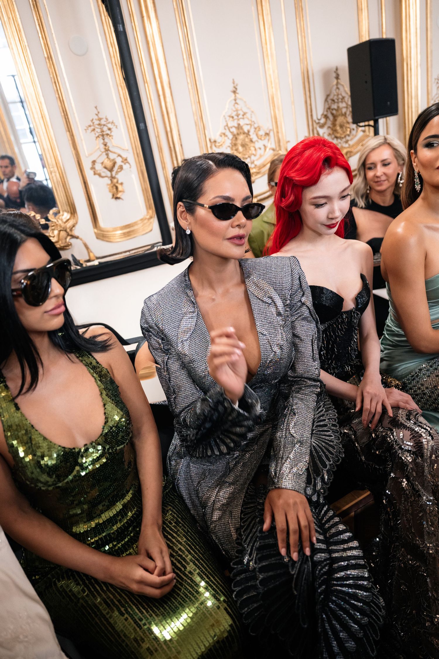 Fashionable guests in glamorous evening wear including sequined dresses and metallic attire at an elegant event in ornate venue.