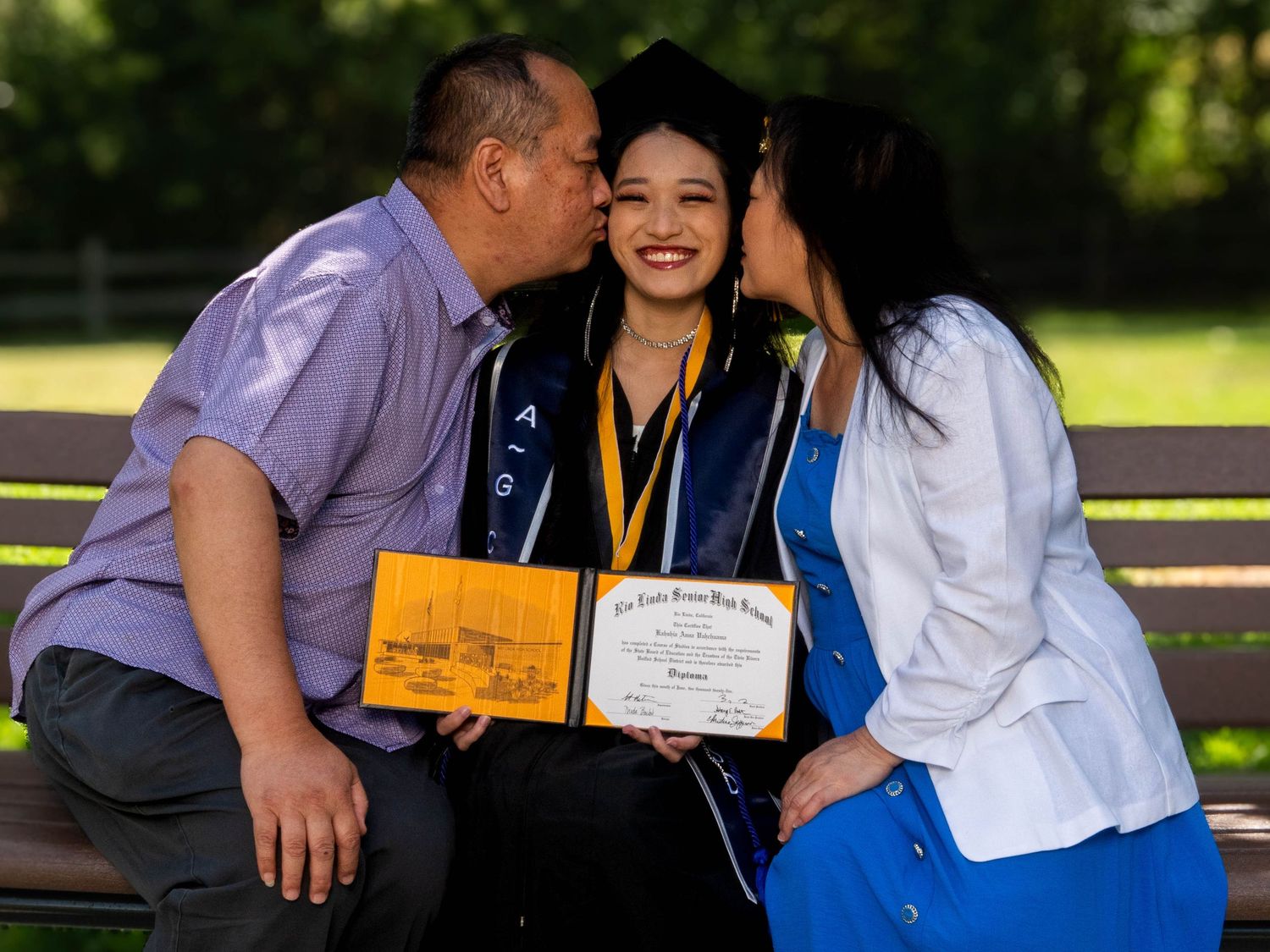 Graduates celebrating with their diplomas in an outdoor garden setting.