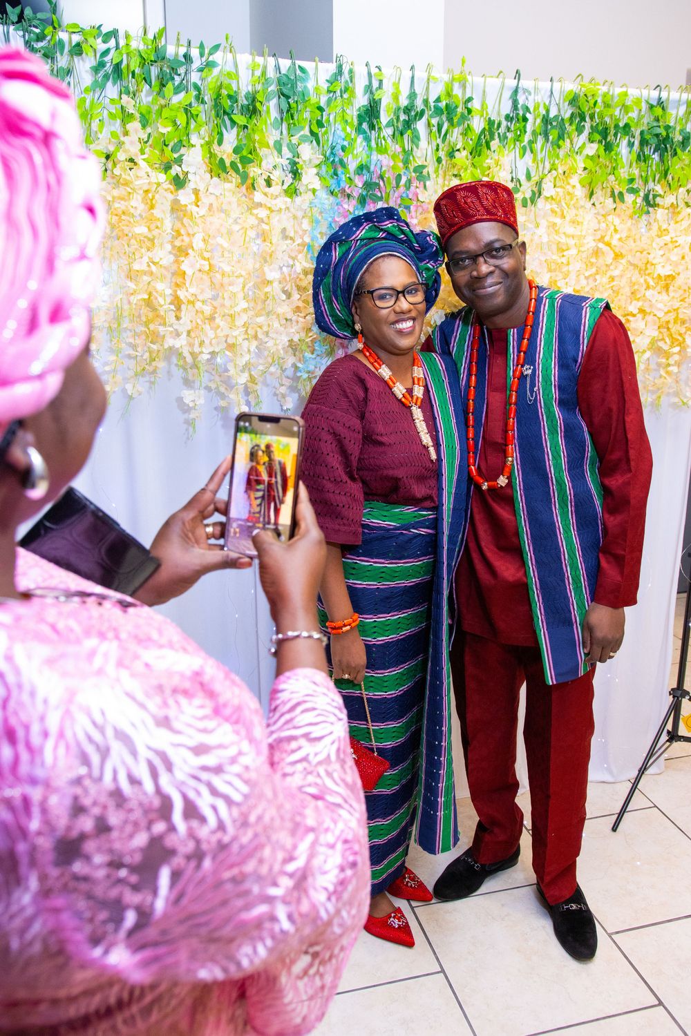 A couple in traditional African attire poses for a photo being taken on a phone at a formal event.