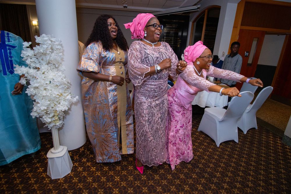 Guests in coordinated purple and pink traditional African attire dance and celebrate at an elegant indoor event.