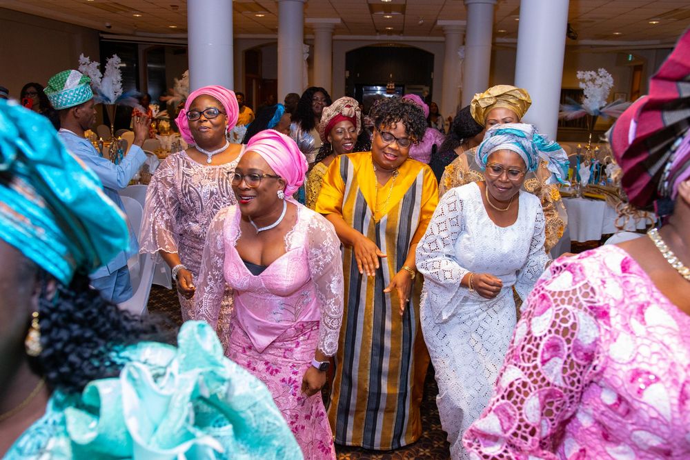 A group celebrates at a traditional African wedding ceremony wearing vibrant pink, blue and yellow attire.
