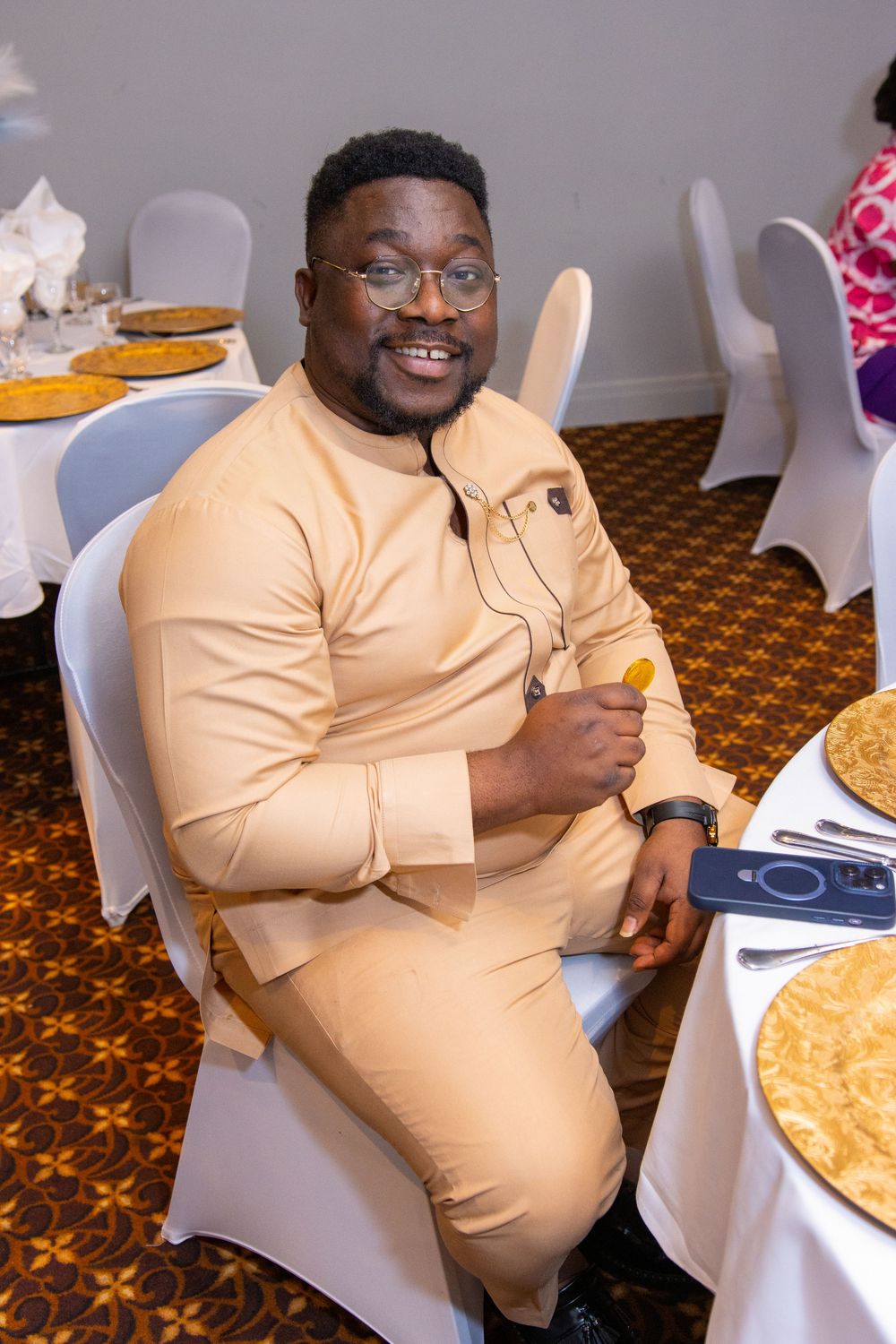 A person in a peach-colored outfit sits at a dining table with pies, giving a thumbs up while wearing glasses.