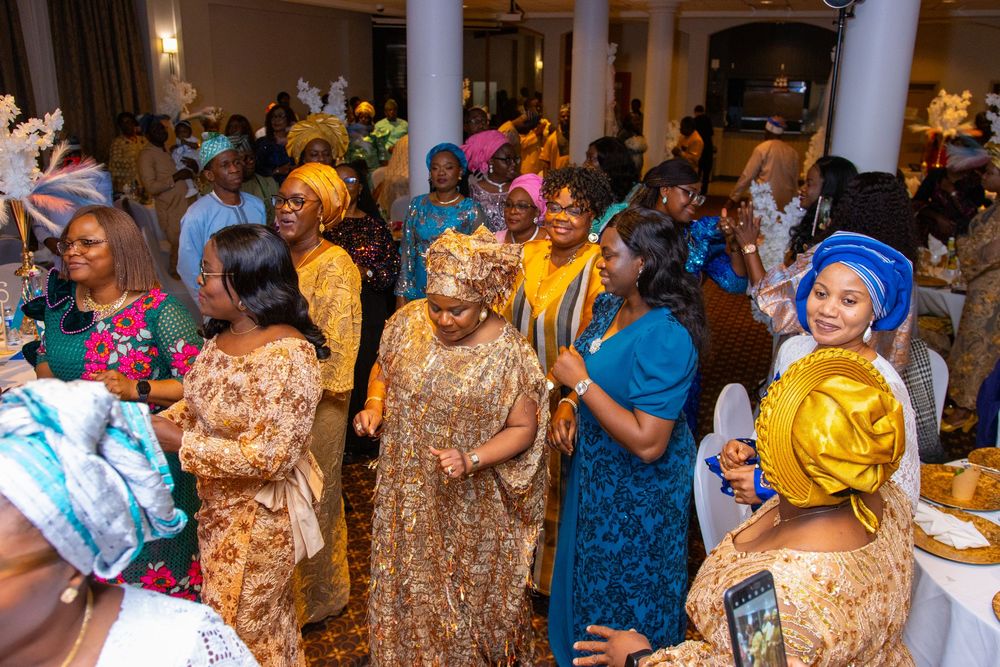 A lively celebration with people dancing and wearing traditional African attire in gold and blue colors at an indoor event.