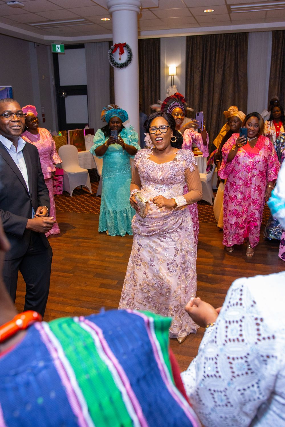 People dancing and celebrating at a formal event wearing colorful traditional African attire in vibrant pinks and teals.