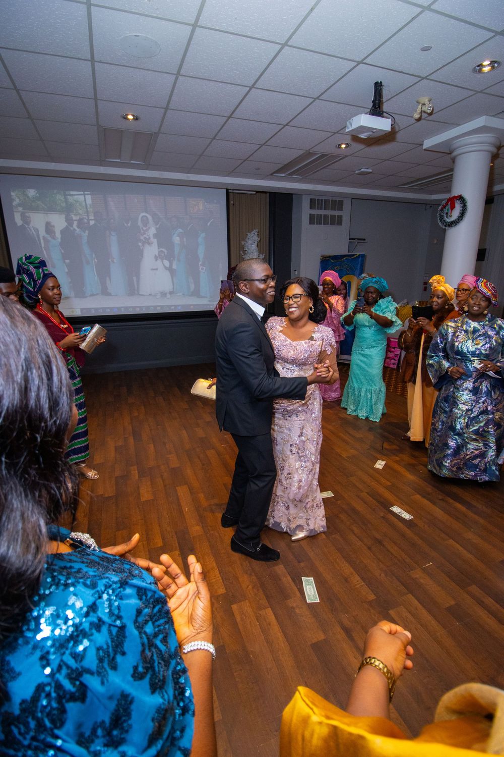 Guests in colorful traditional attire celebrate at a wedding reception as a couple dances in the center of the room.