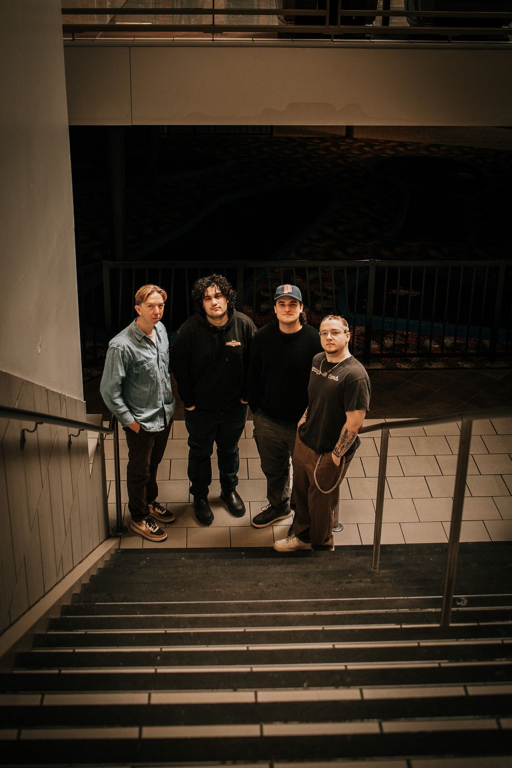A group of four people standing on concrete stairs in casual attire with moody lighting.