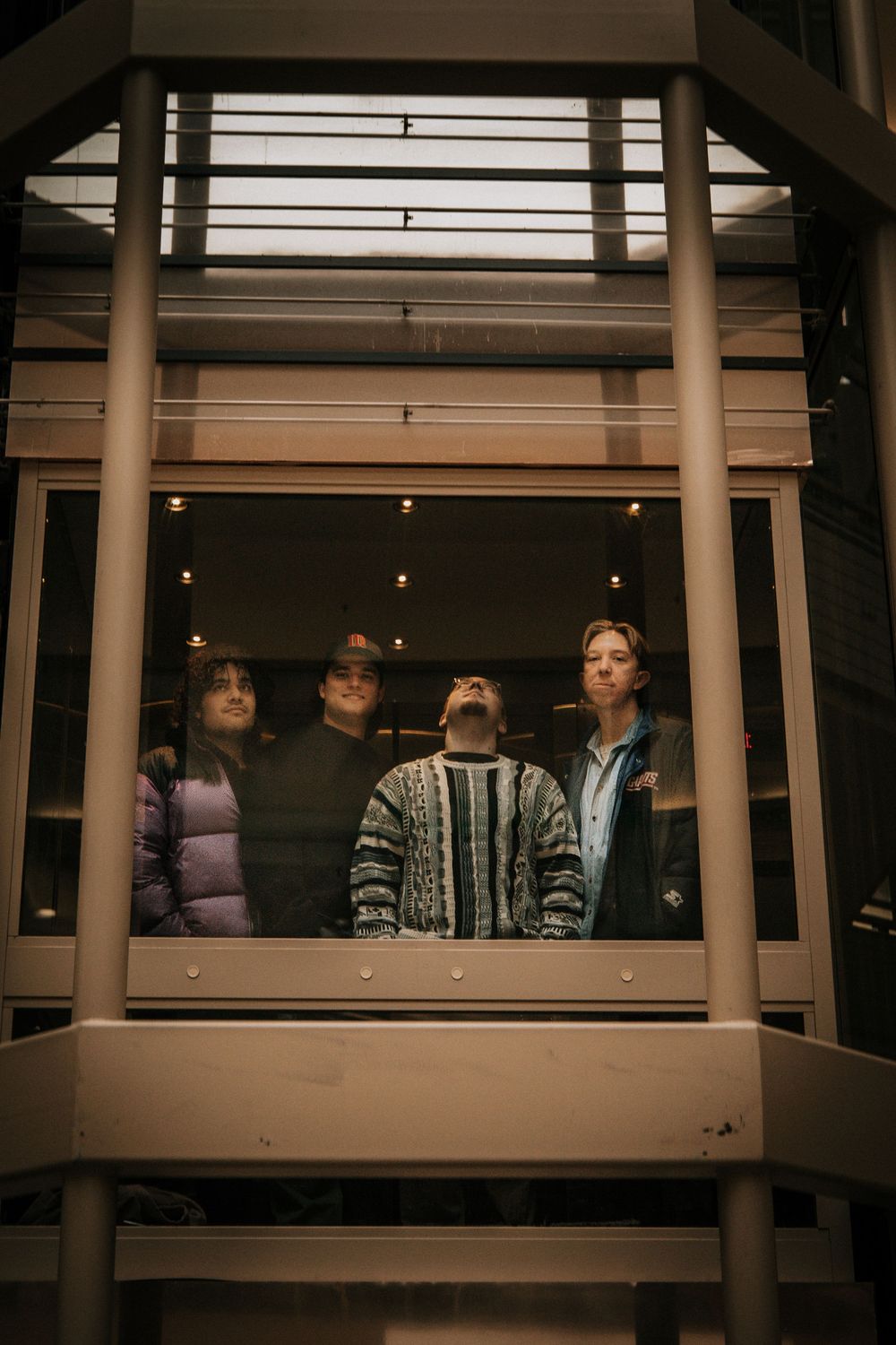 Four people stand together looking up through a window frame at night with moody lighting and architectural elements.