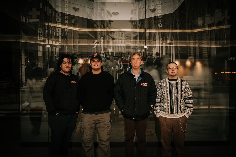 A group stands together in a dimly lit industrial space with dark walls and dramatic lighting.
