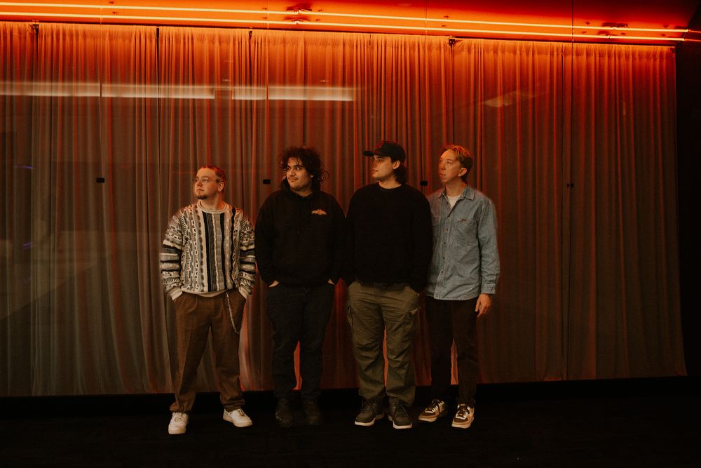 Four people standing in front of a red-lit curtain backdrop in an indoor setting.