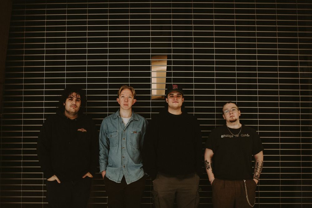 A group of people pose together in front of a dark wall with horizontal blinds in a dimly lit setting.