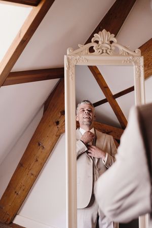 An ornate white decorative frame hangs on a wall with exposed wooden beams in an interior setting.