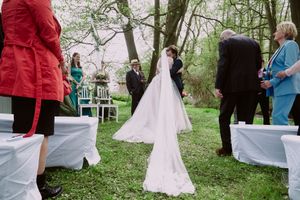 A wedding ceremony takes place outdoors in a garden setting with guests gathered around.