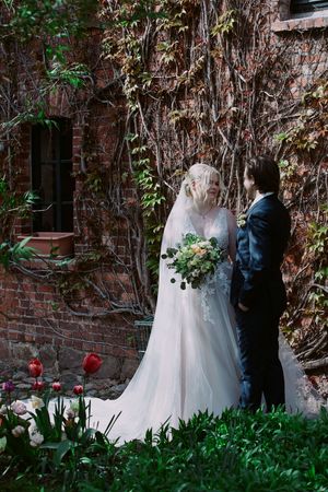 A wedding couple poses against a rustic brick wall covered in climbing vines.