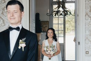 A couple in formal wedding attire stand in an elegant doorway with natural light streaming in.