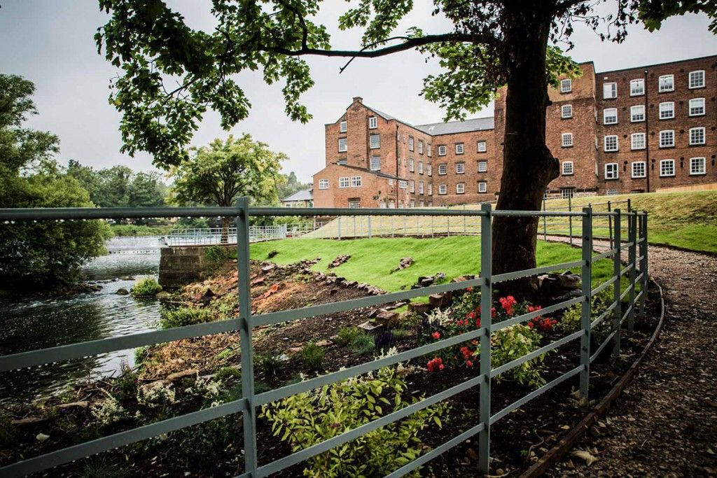 Panoramic view of brick buildings and waterways surrounded by green trees.