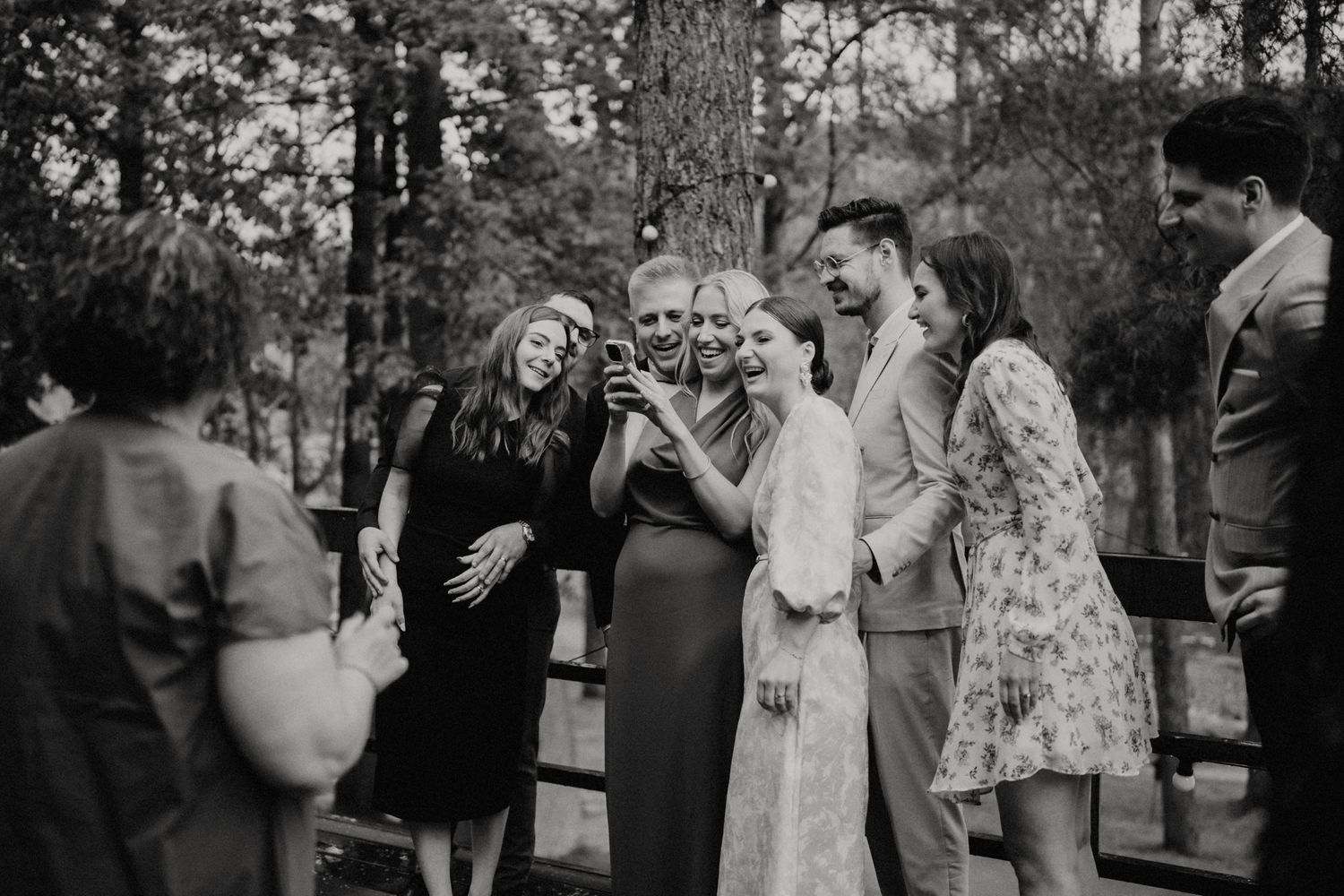 Wedding guests gather in a wooded outdoor setting for celebrations.