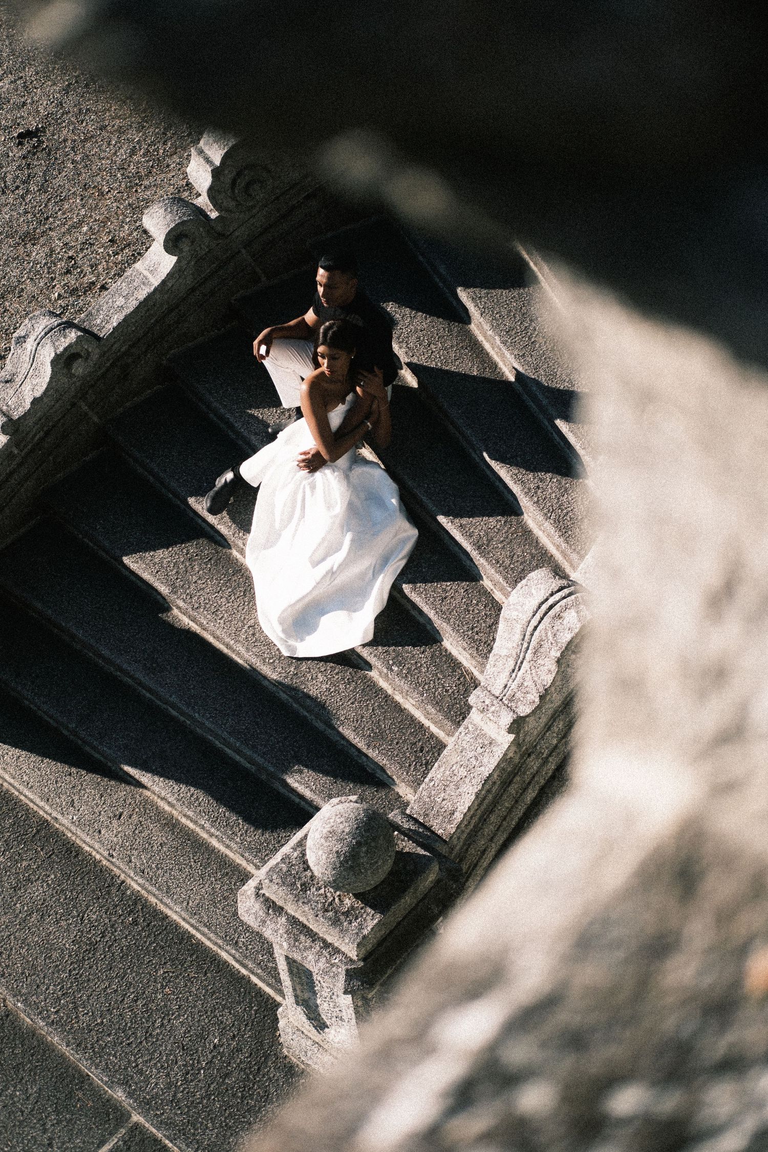 Overhead view of a person in white clothing walking across a textured concrete surface casting dramatic shadows.