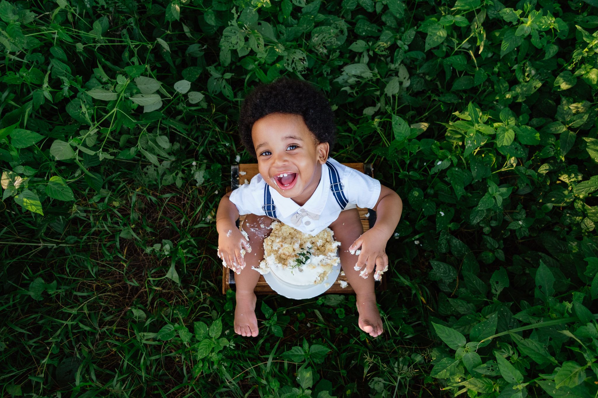 One-year-old smashing a cake and laughing, surrounded by greenery