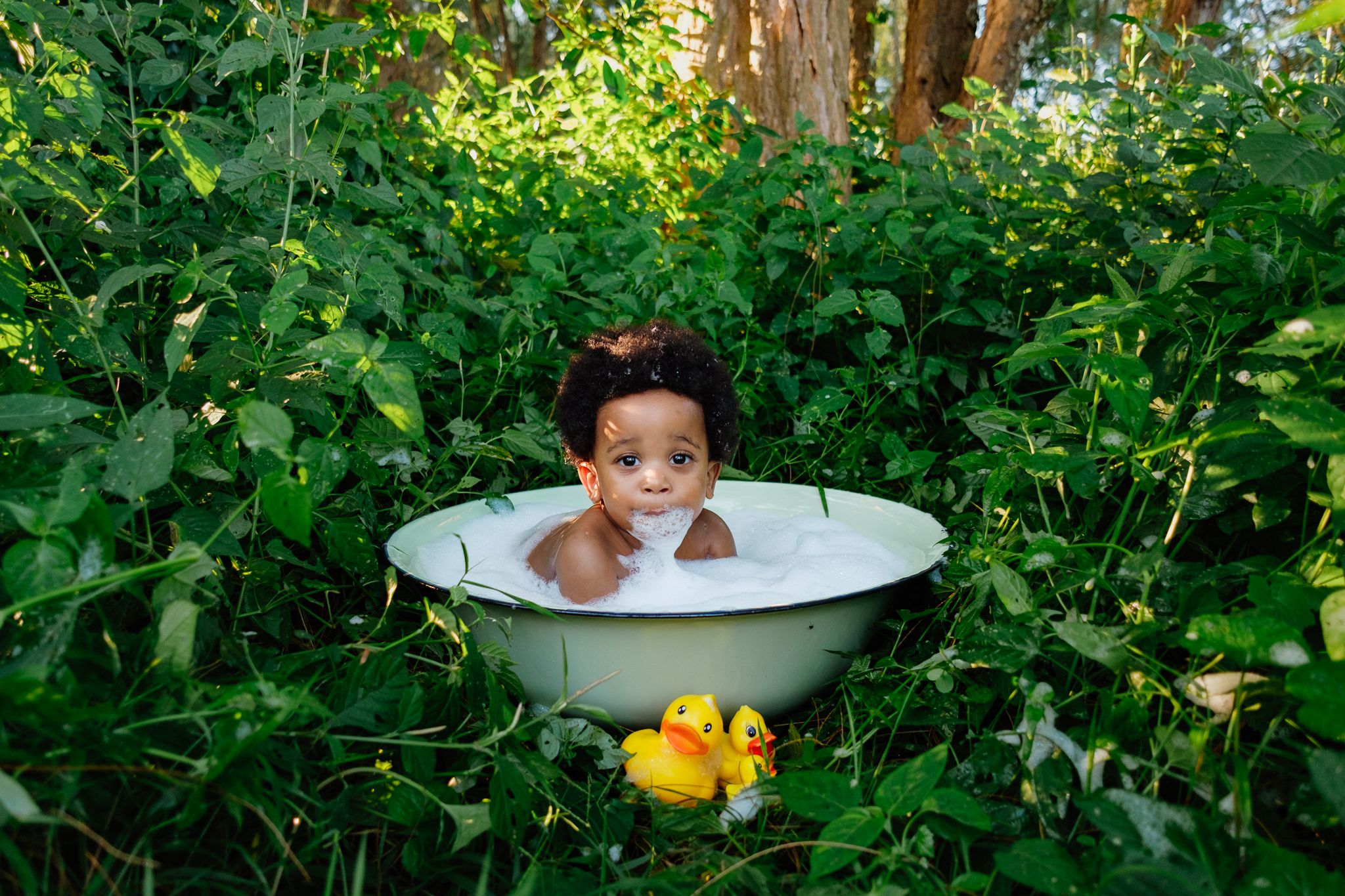 Little boy in a bubble bath with ducks and a bubble beard in a forest setting