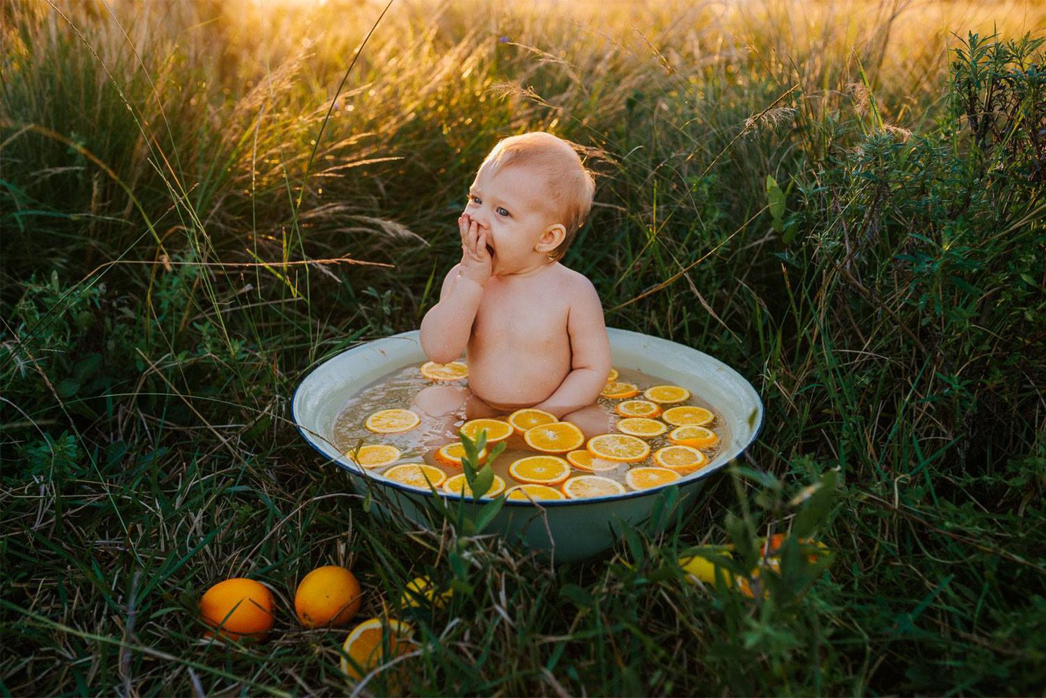 One-year-old baby enjoying a fruit bath backlit by warm sunlight