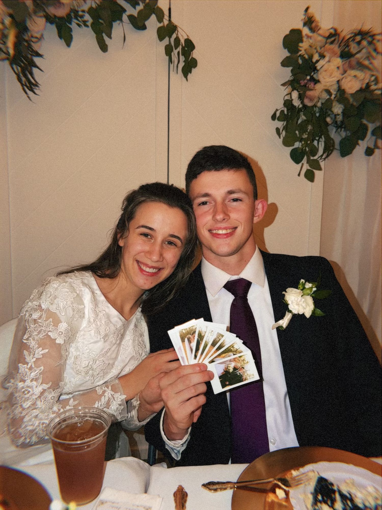 Wedding reception scene with couple sharing candid moments and holding photos.