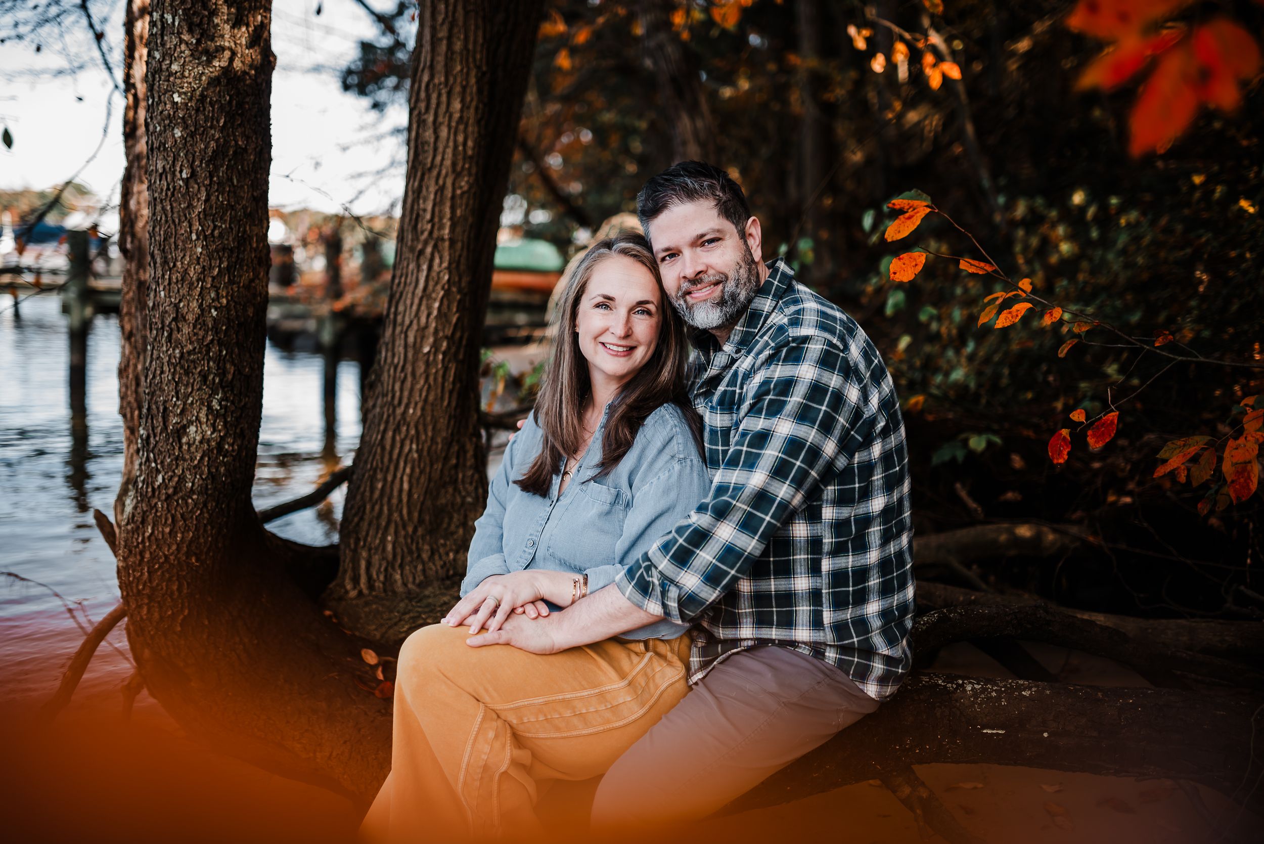 Couple sitting close together on wooden steps surrounded by autumn foliage and trees.