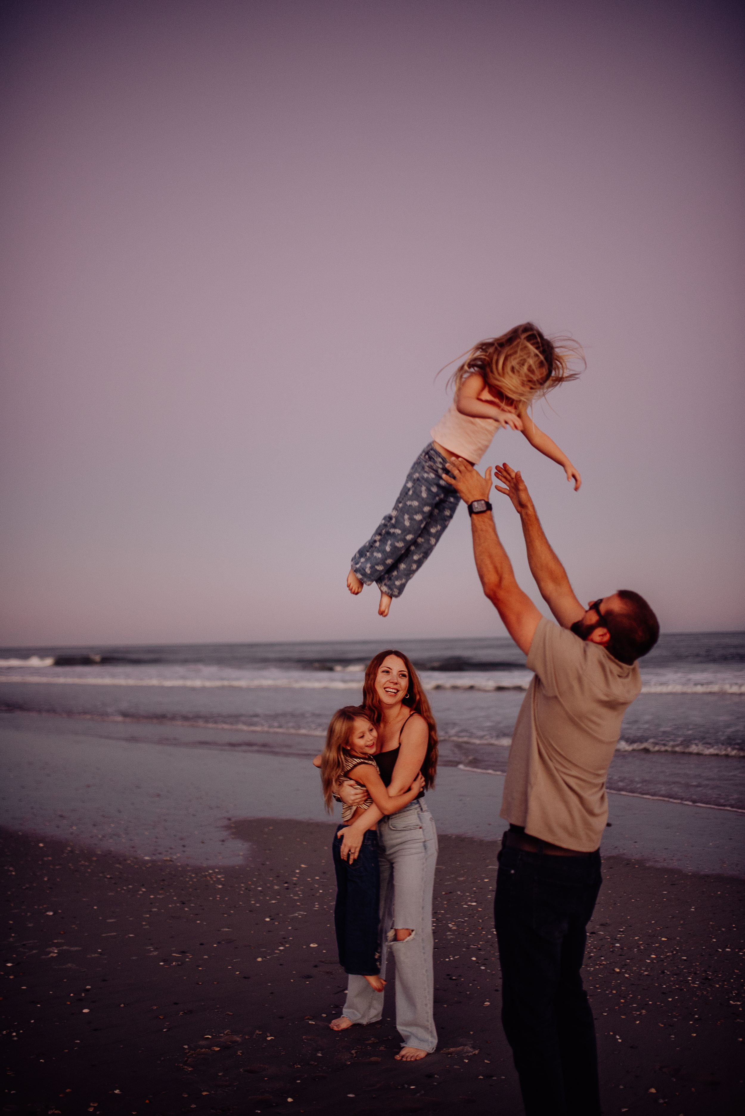 Family plays and dances together on a misty beach at sunset in a series of candid moments.