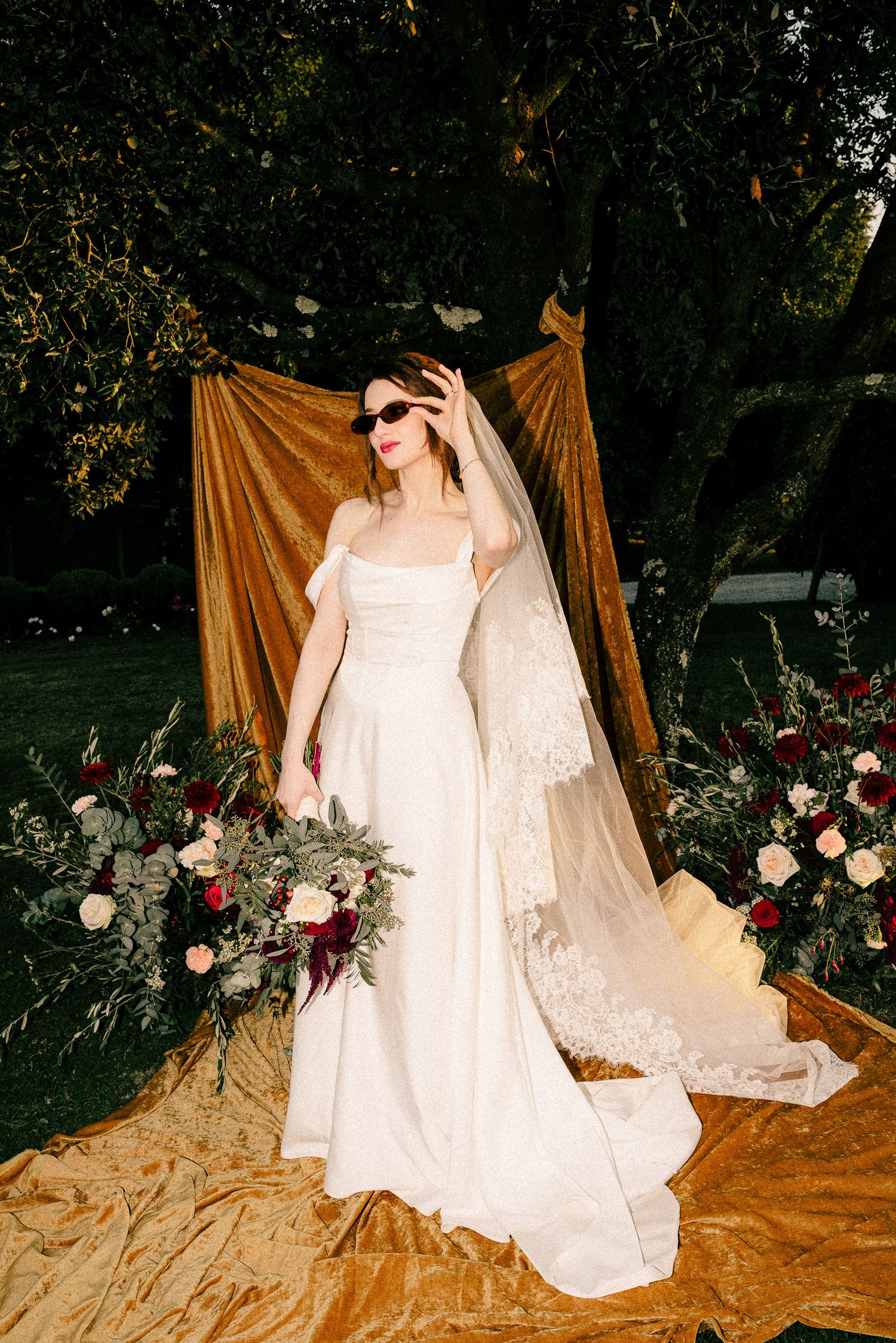 A bride in a classic white wedding dress poses gracefully against a golden backdrop with floral arrangements.
