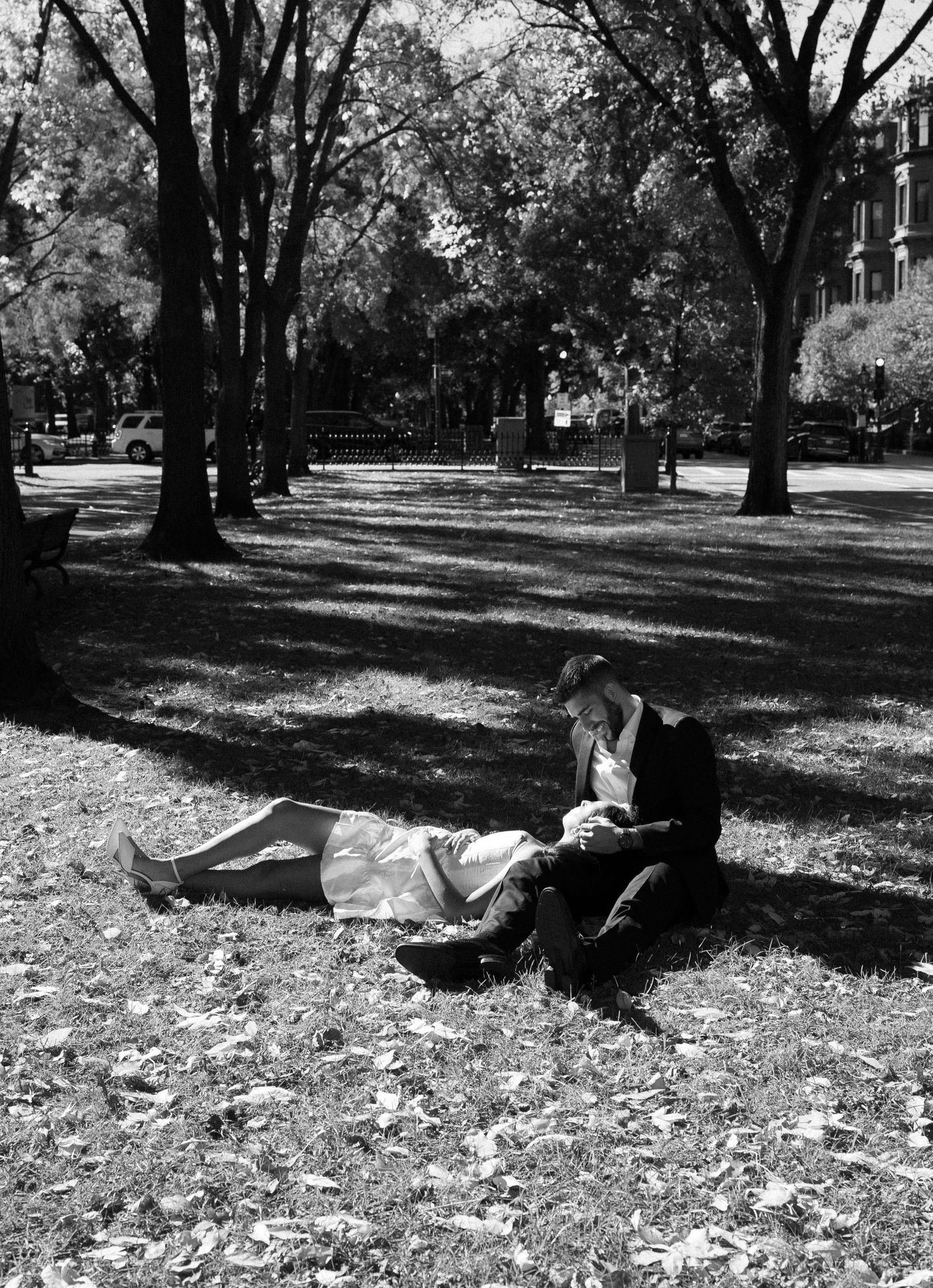 A sequence of black and white photos shows someone lying on autumn leaves in a park beneath tall trees in Boston