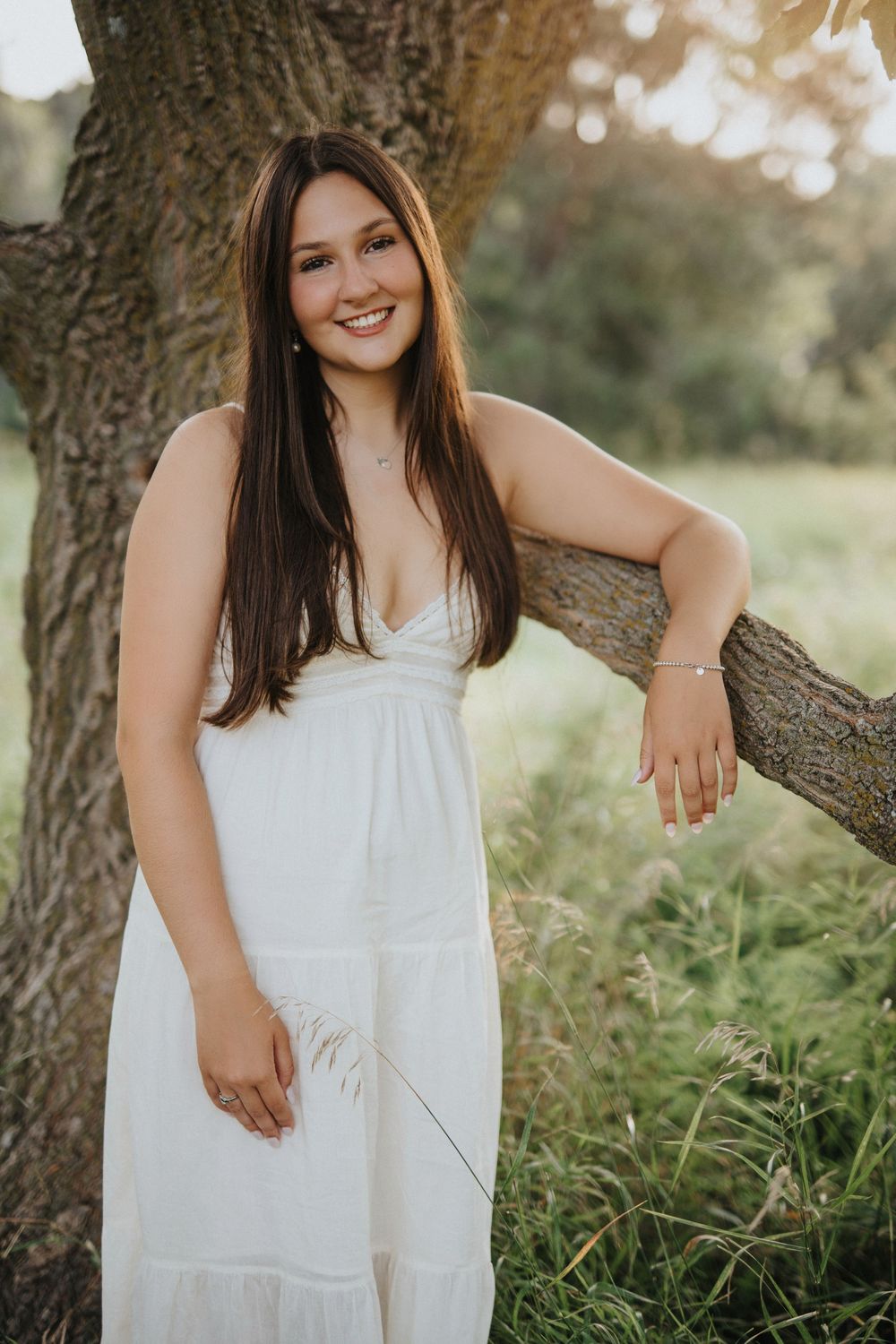 A white sundress stands out against a natural outdoor setting with tall grass and trees in golden afternoon light.