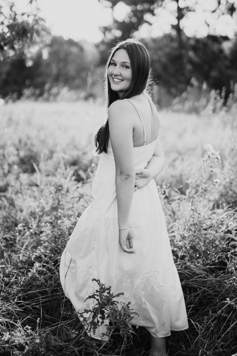A black and white photo series shows someone in a white dress sitting and walking through a wildflower meadow.