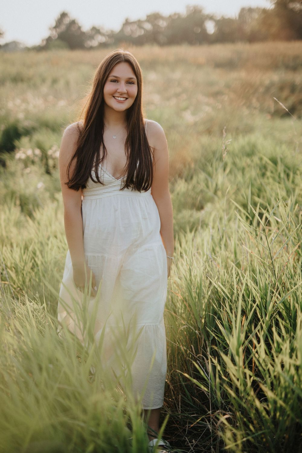Ethereal portrait in a white dress among tall grass during golden hour with soft natural lighting.