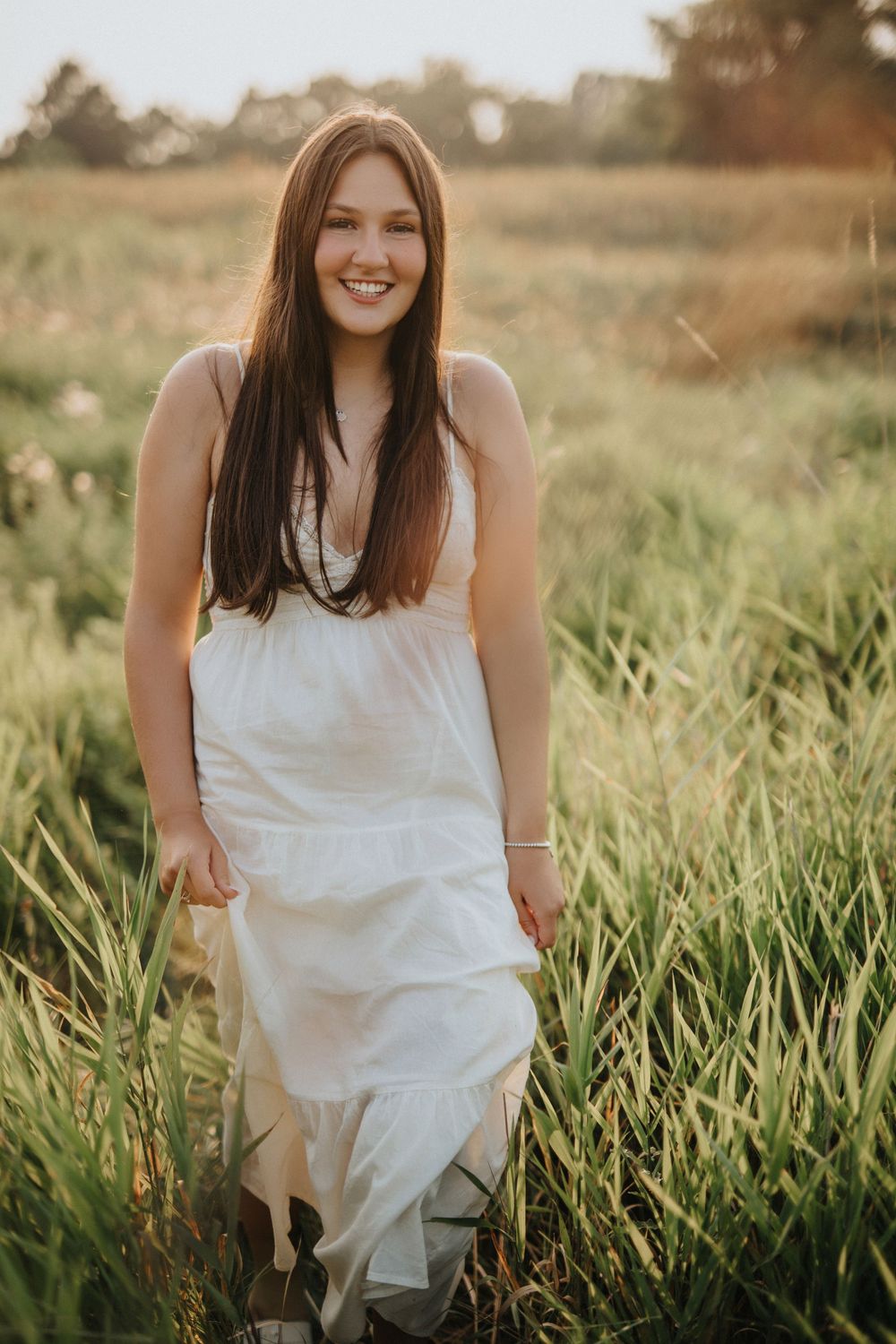 A flowing white dress catches sunlight as someone moves through a field of tall grass at sunset.